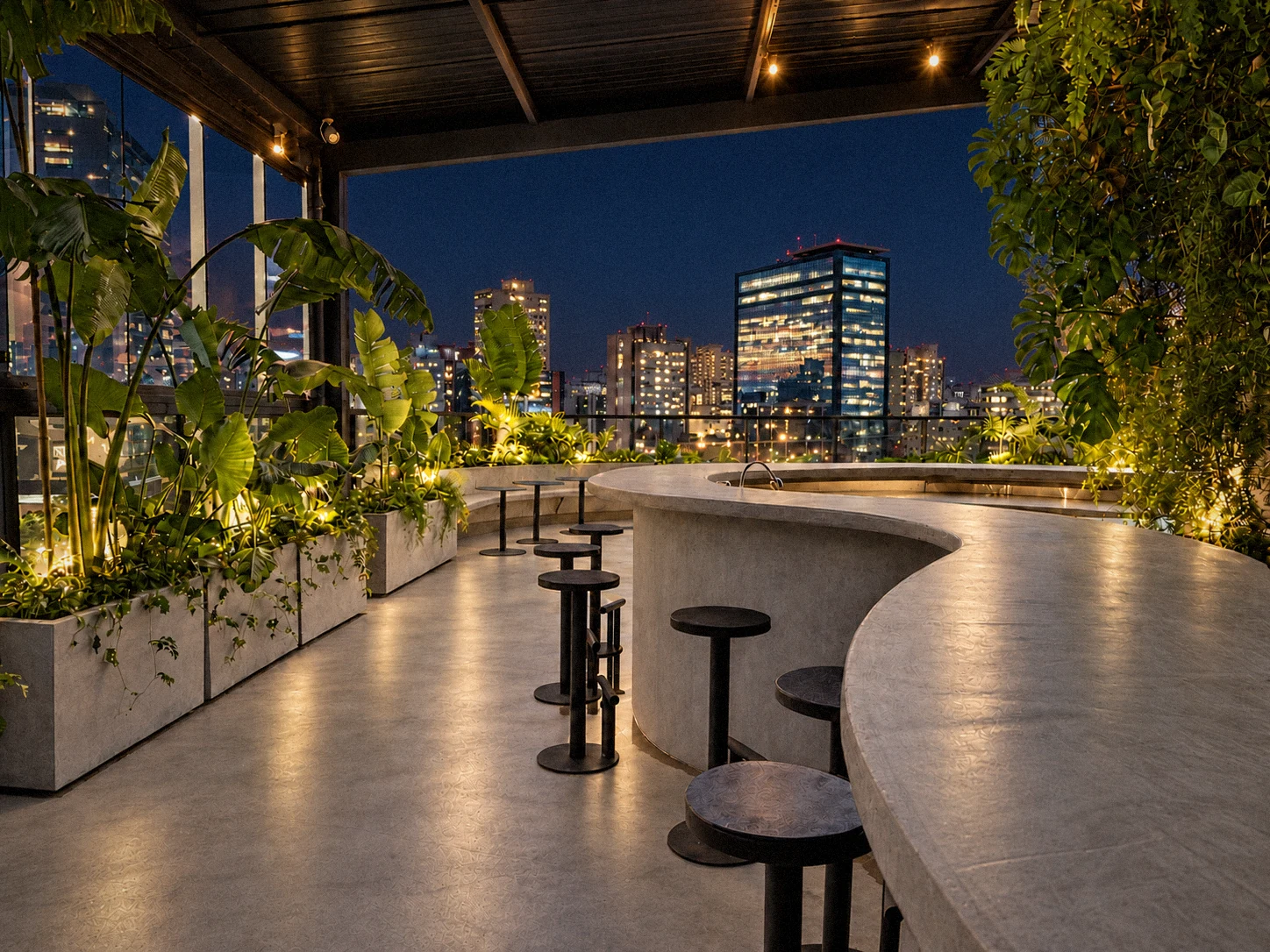 Rooftop à noite, com balcão curvo, plantas iluminadas e a cidade acesa ao fundo