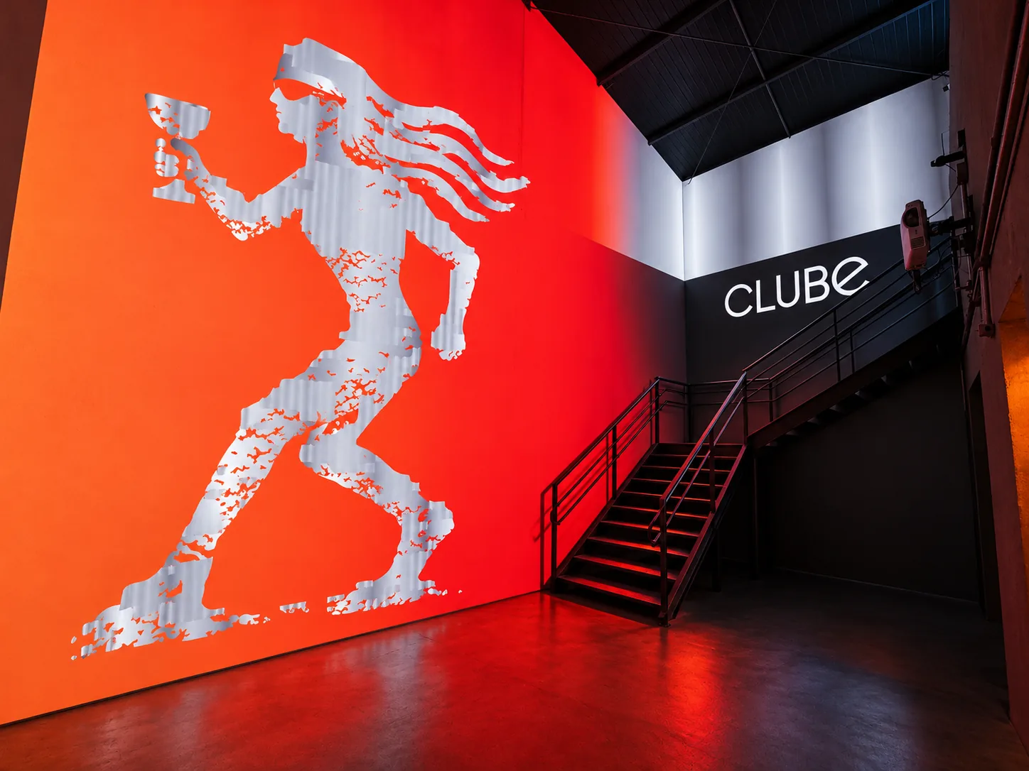 Sala imersiva com personagem do CLUBE projetado sobre gradiente vermelho