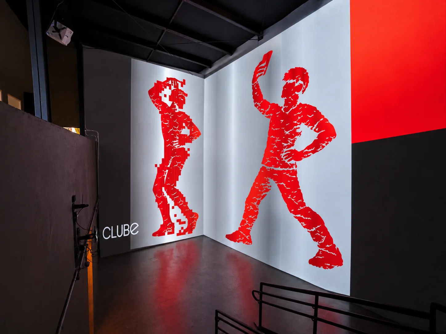 Sala imersiva com dois personagens do CLUBE em vermelho projetados sobre metal